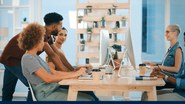 A group of diverse people in an office, gathered around a table and having a pleasant interaction.