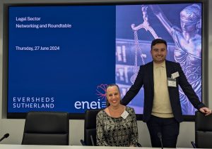 Sandi and Jack with big happy smiles as they stand in front of a big screen displaying the title screen of a roundtable event.